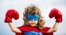 Child in superhero cape and red boxing gloves standing confidently.