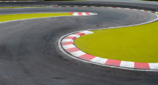 Curved race track with red and white kerbs and green runoff area.